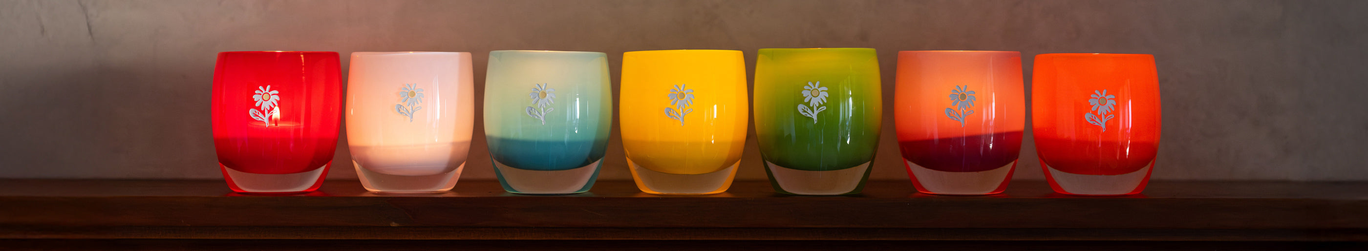 bloom collection. colorful glassybaby lined up on shelf.