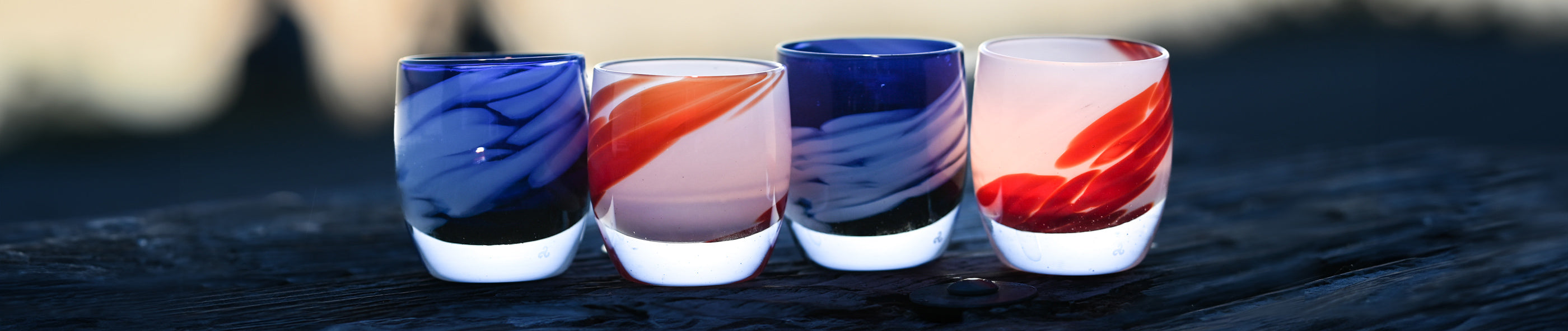 'free bird' and 'maverick' red white and blue glassybaby sitting on wood rail at sun set