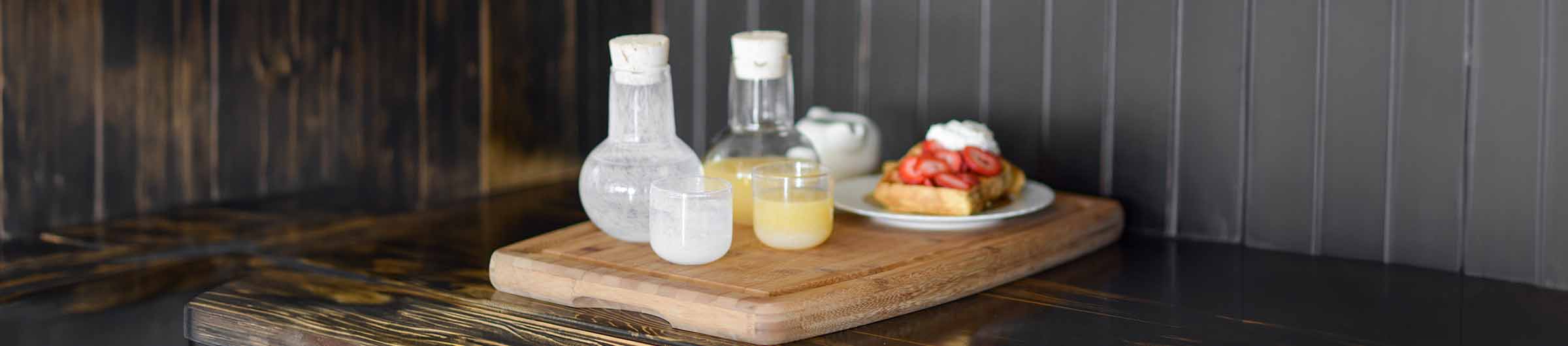 clear and white glass sipper sets filled with water and orange juice on a wood serving board with a plate of sweet waffles.