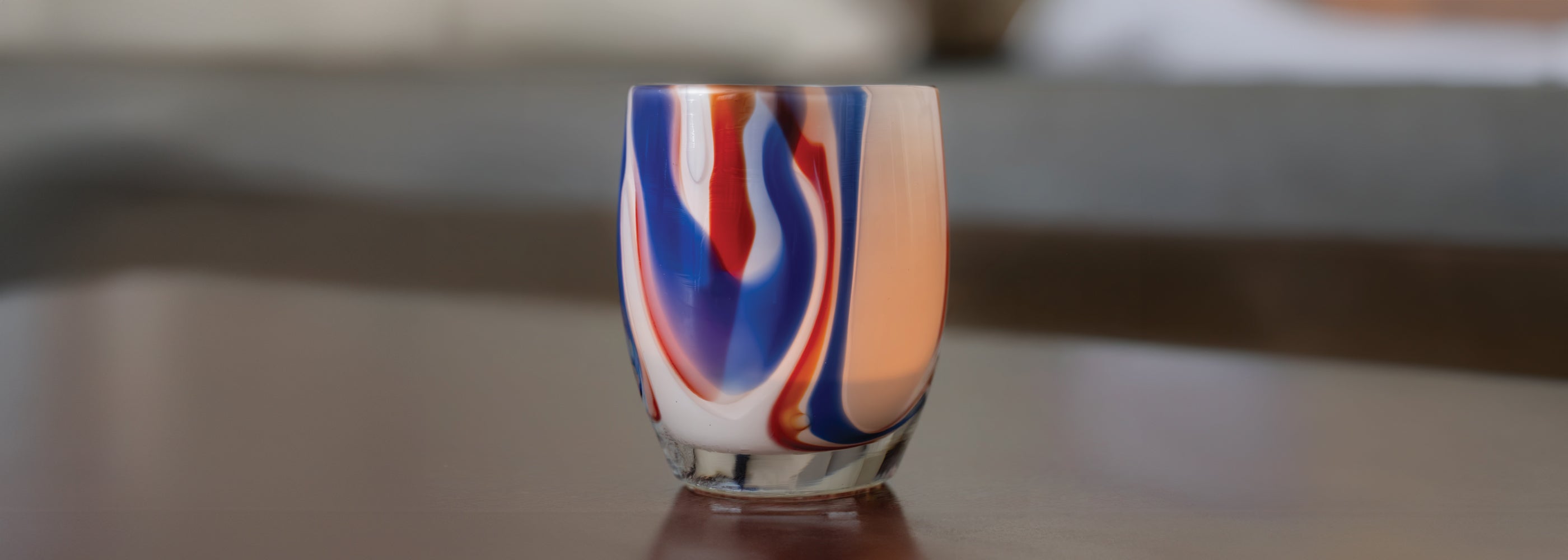 250th, red white and blue swirl glass candle holder on a reflective surface with a blurred background