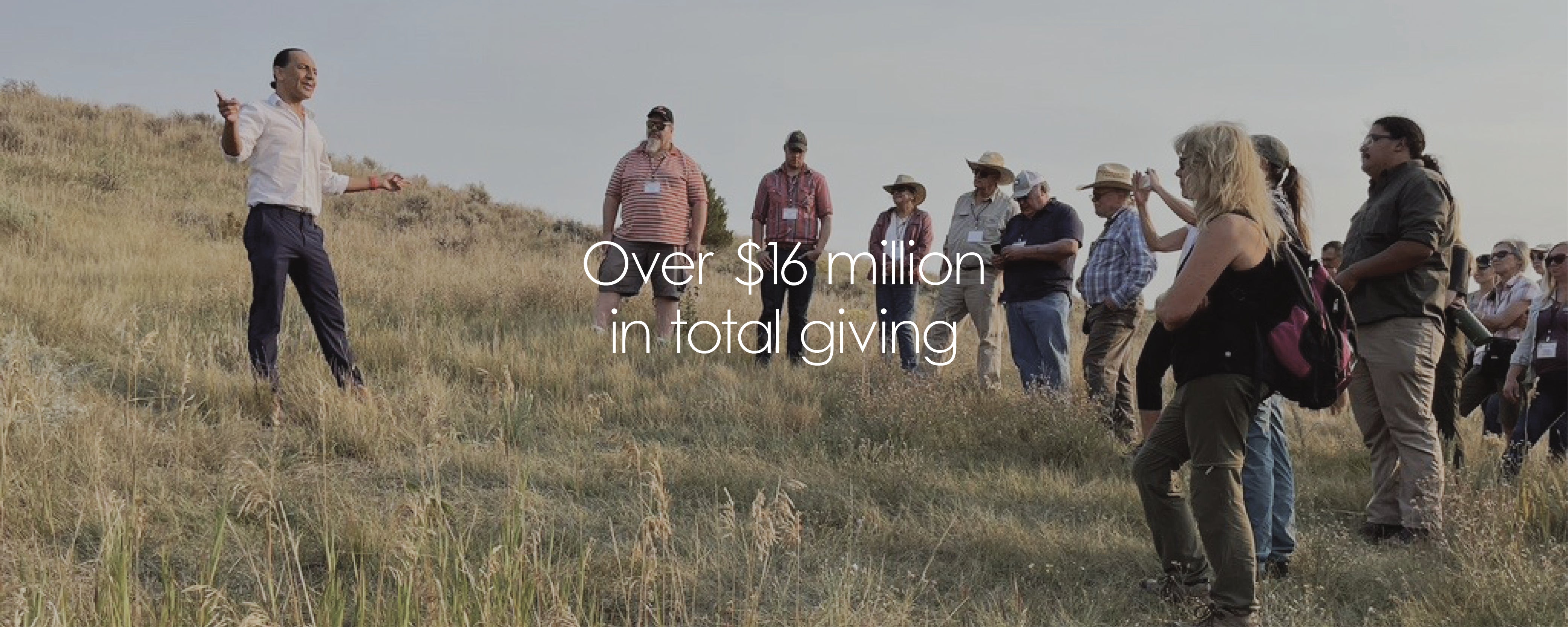 Group of people standing on a grassy hill with text overlay about total giving amount.