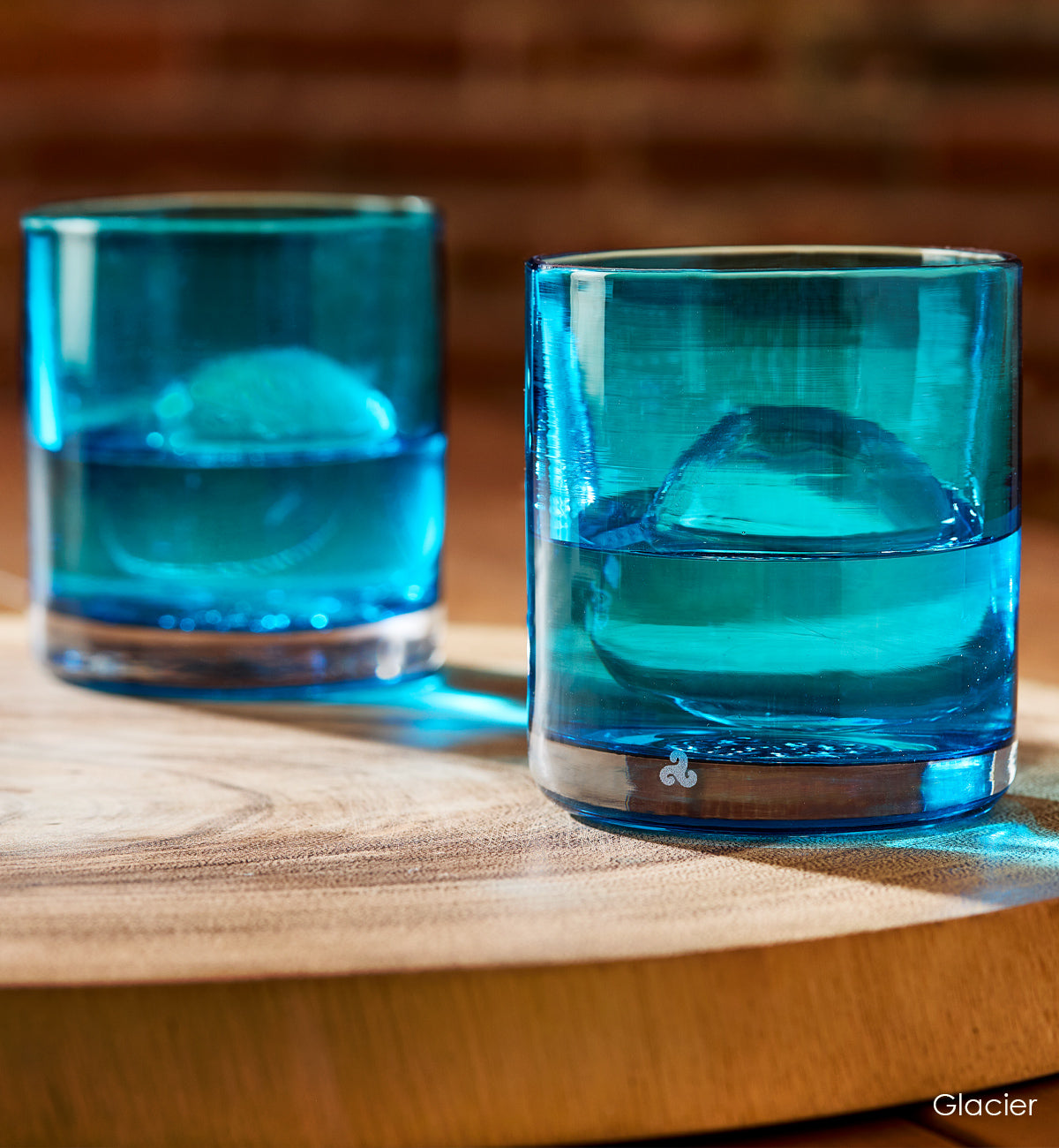 two Glacier rockers, light blue transparent hand-blown glass lowball drinking glasses with ice and liquid on top of wood table.