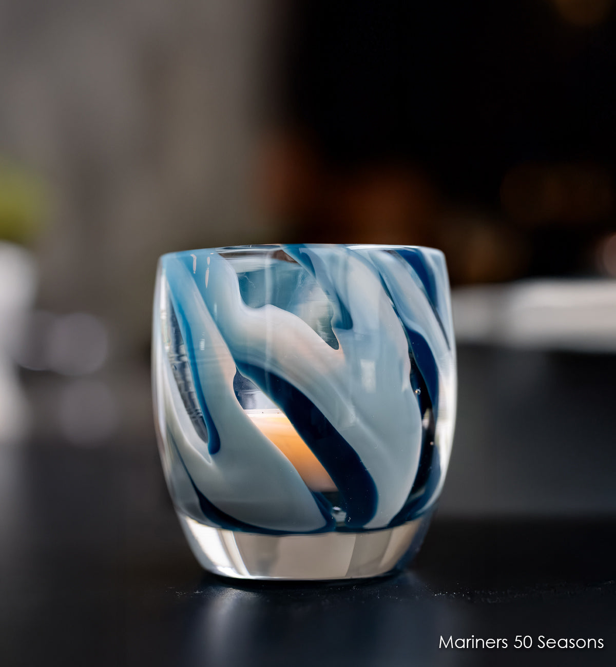 Mariners 50 Seasons glass votive candle holder with blue and white swirl design on a dark surface.