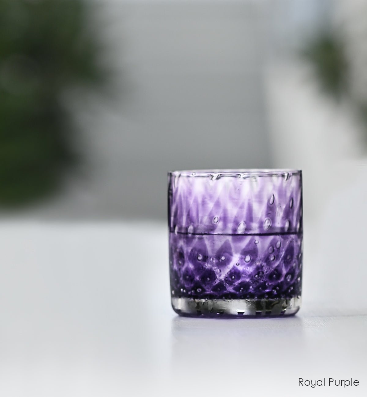 royal purple rocker, purple with bubble pattern hand-blown glass lowball drinking glasses on a white surface with plants in background.