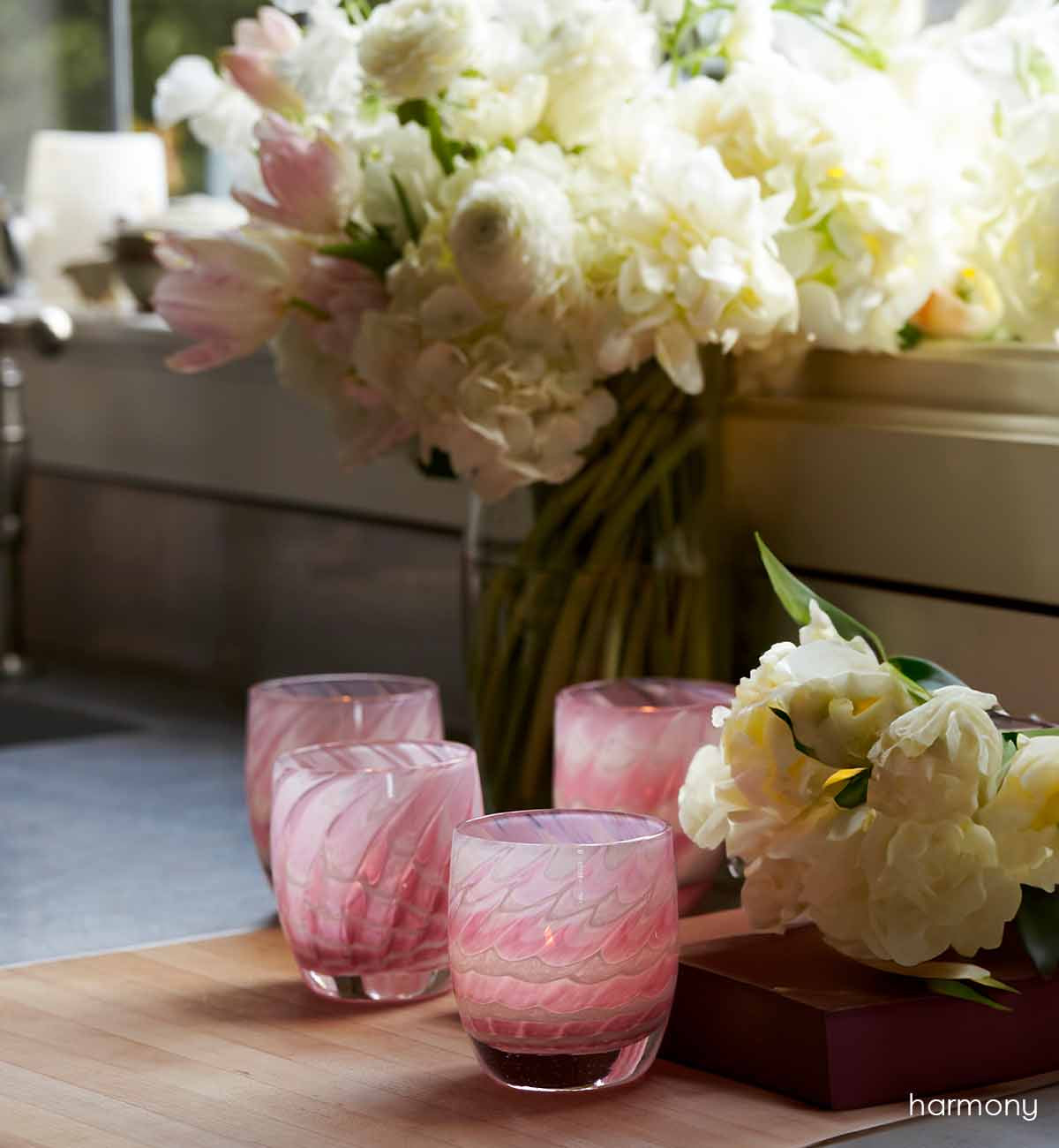 harmony, pink feathered texture hand-blown glass votive candle holder. In a lit kitchen display with a white bouquet.