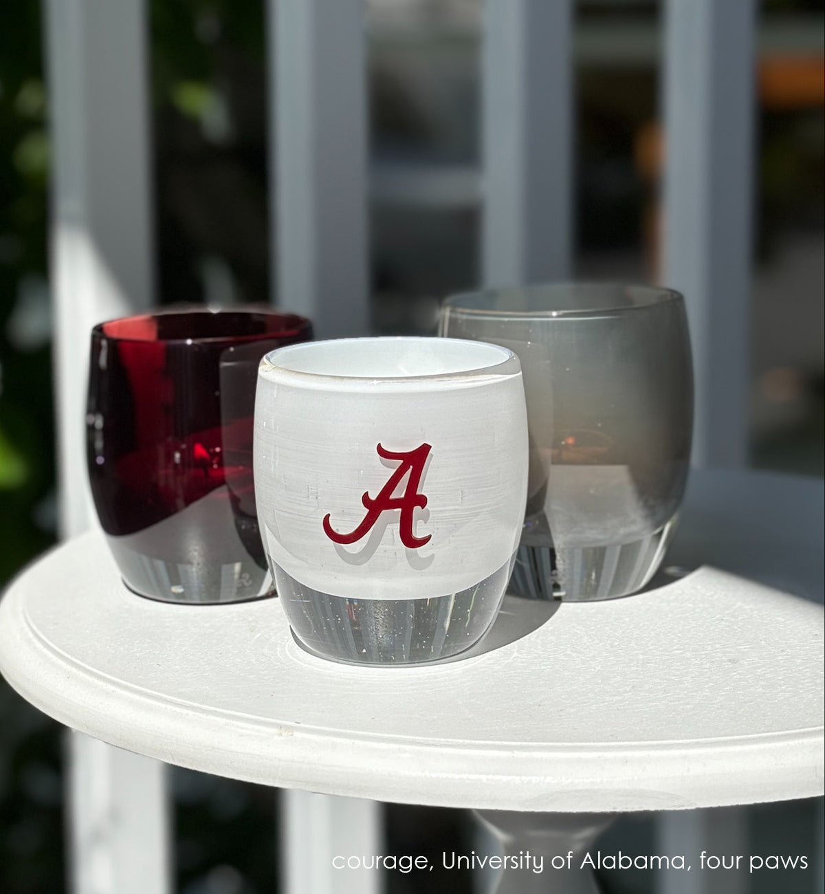 etched University of Alabama college logo on a white hand-blown glass candle holder sitting on a white table with a courage and four paws glassybaby.