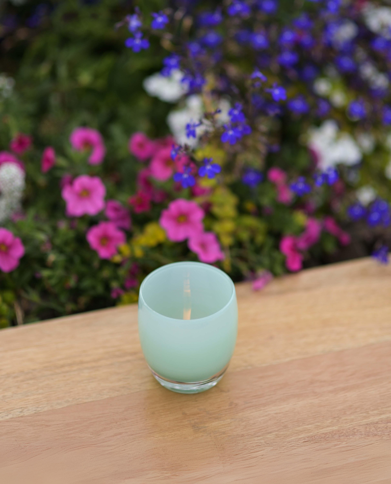 thank you, light green hand-blown glass candle holder sitting on a wood table with flowers in the background.