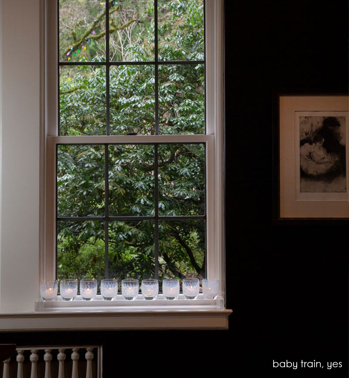 clear baby train™ nine well stand for hand-blown glass votive candle holders holding yes, placed on a white windowsill in a navy blue painted room.