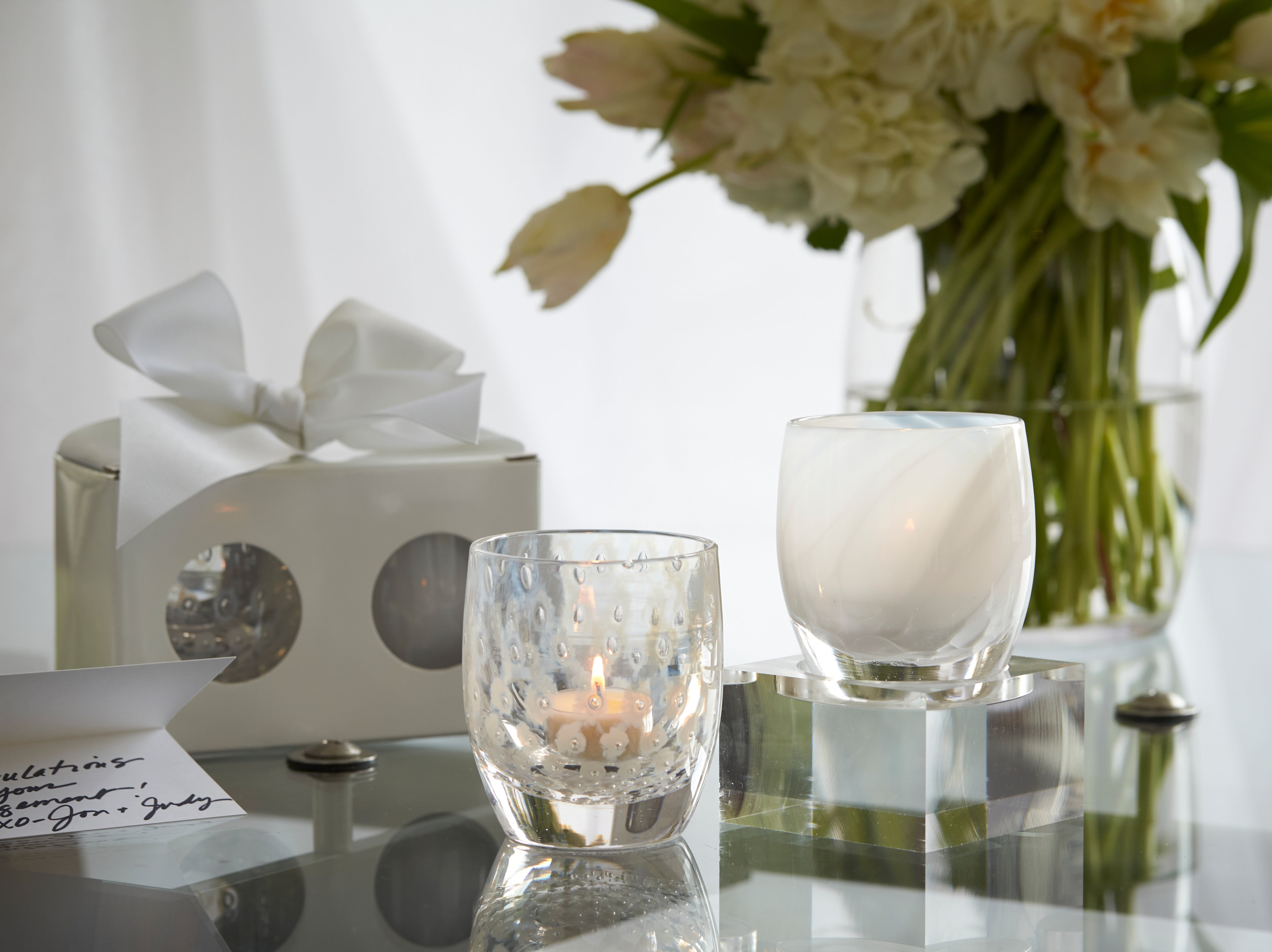 become one set, glassybaby yes and embrace sitting on a glass table with a wrapped become one set, notecard and vase of flowers.