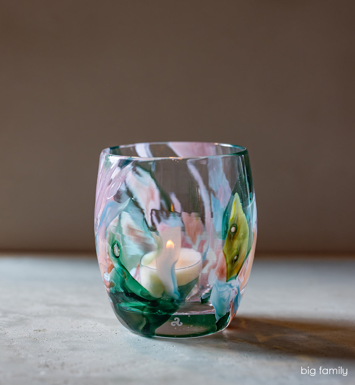 'big family' multi-color (pinks, greens, light blues) hand-blown glass candle holder on tan table with light brown background