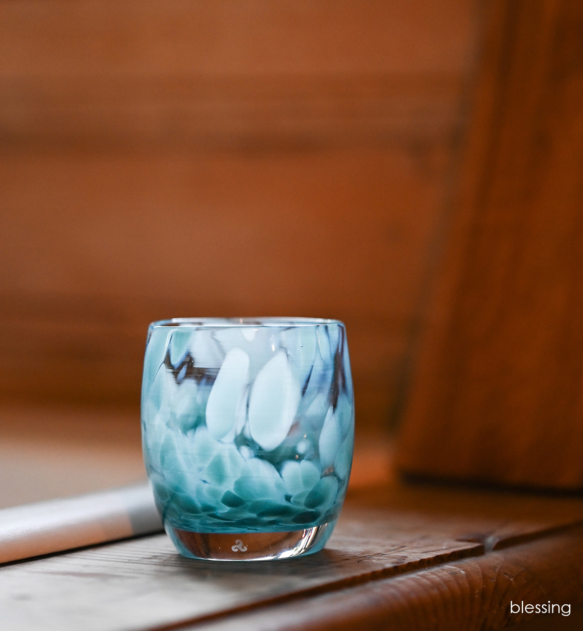 blessing light blue petal patterned, hand-blown glass votive candle holder on a wood surface sitting in natural light.