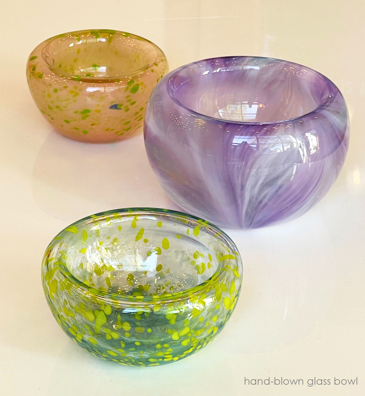 Three hand-blown glass bowls with different colors and patterns on a white background.
