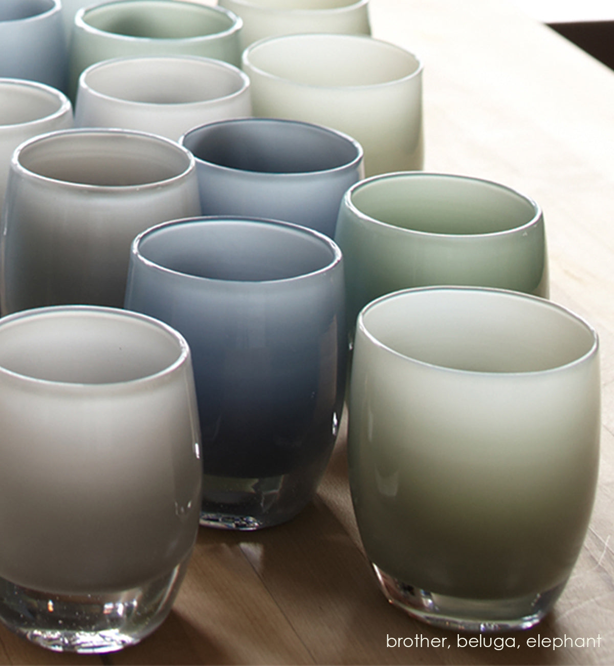 several brother smokey gray hand-blown glass votive candle holders grouped with beluga and elephant on a light wood table.