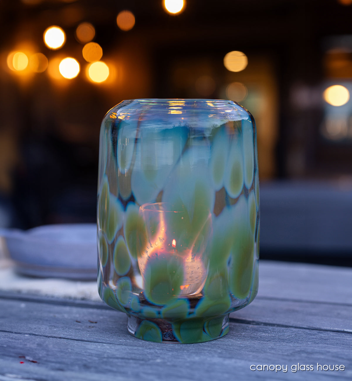canopy glass house, hand-blown glass hurricane with glassybaby in it one wood table at night.