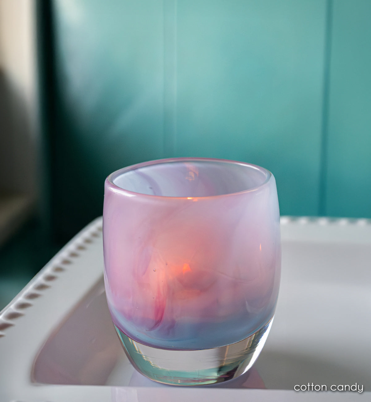 pink purple and blue hand-blown glass candle holder on a white plate with teal background