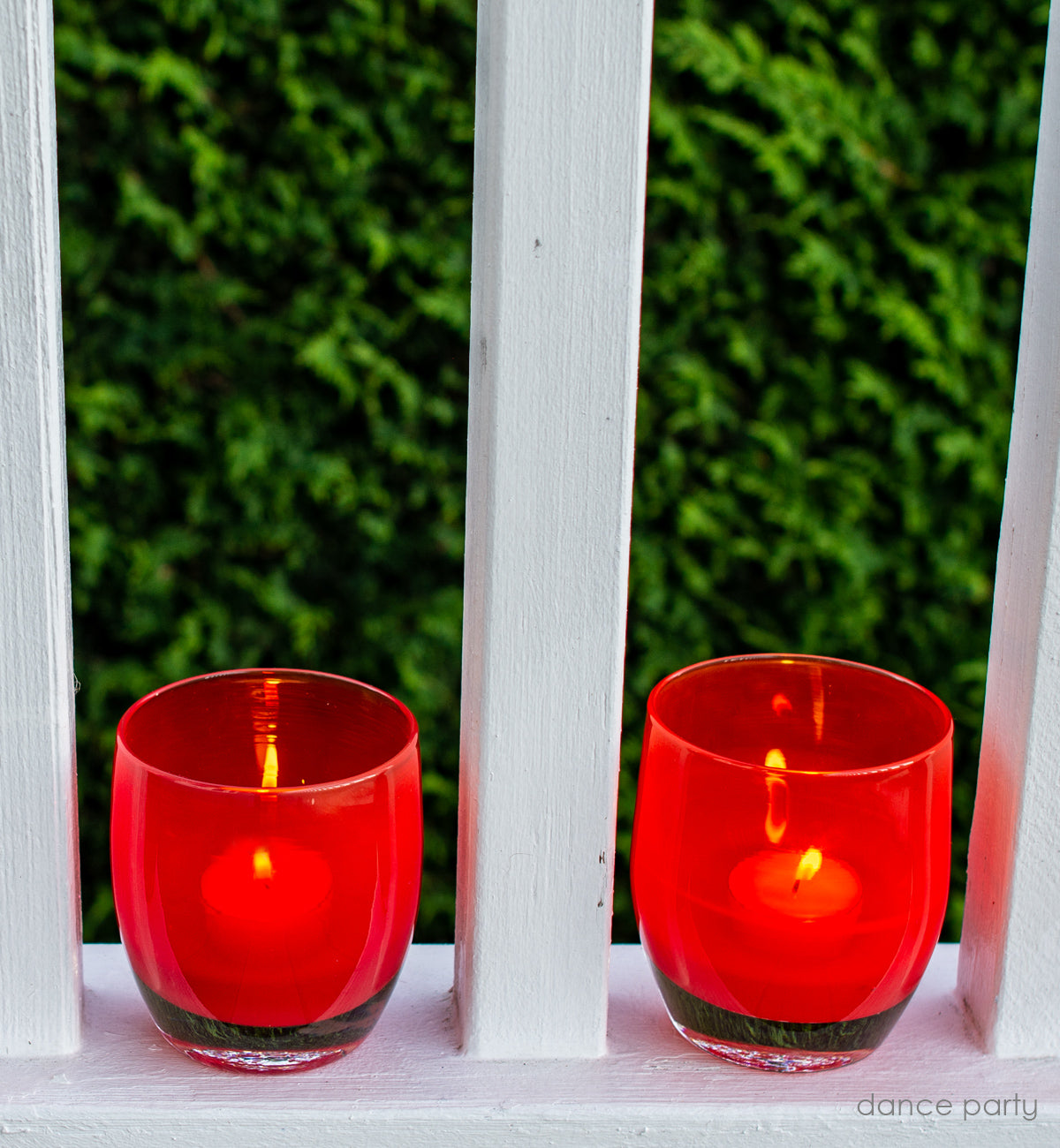 dance party ginger red, hand-blown glass votive candle holder placed between white rails on the porch.