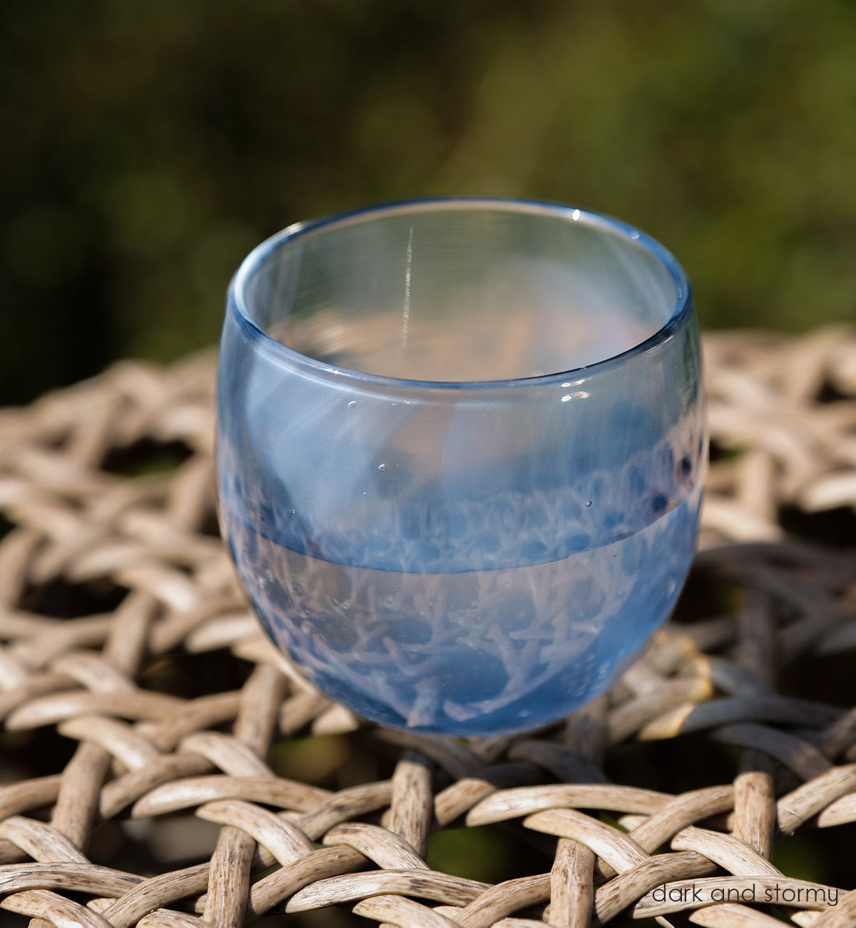dark and stormy deep blue and white swirled together, to create this one-of-a-kind hand-blown drinking glass sitting on a wicker table.