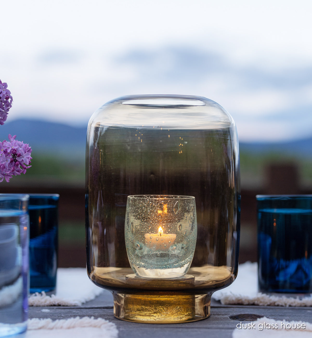 dusk glass house, hand-blown glass hurricane with glassybaby in it one wood table at night.