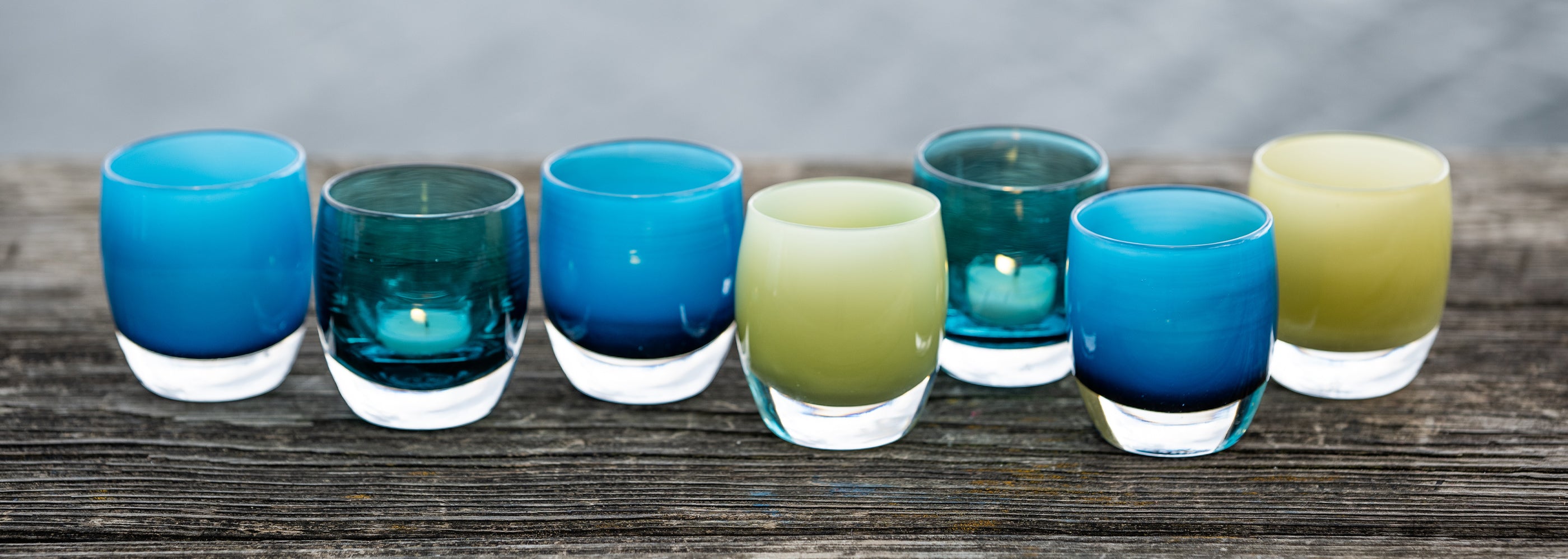 Set of colorful glass votive holders on a wooden surface with a neutral background