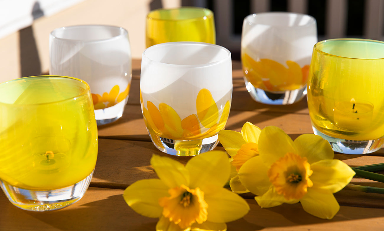 sunflower and buttercup, bright yellow hand-blown glass candle holders sitting on a wooden table with fresh daffodils