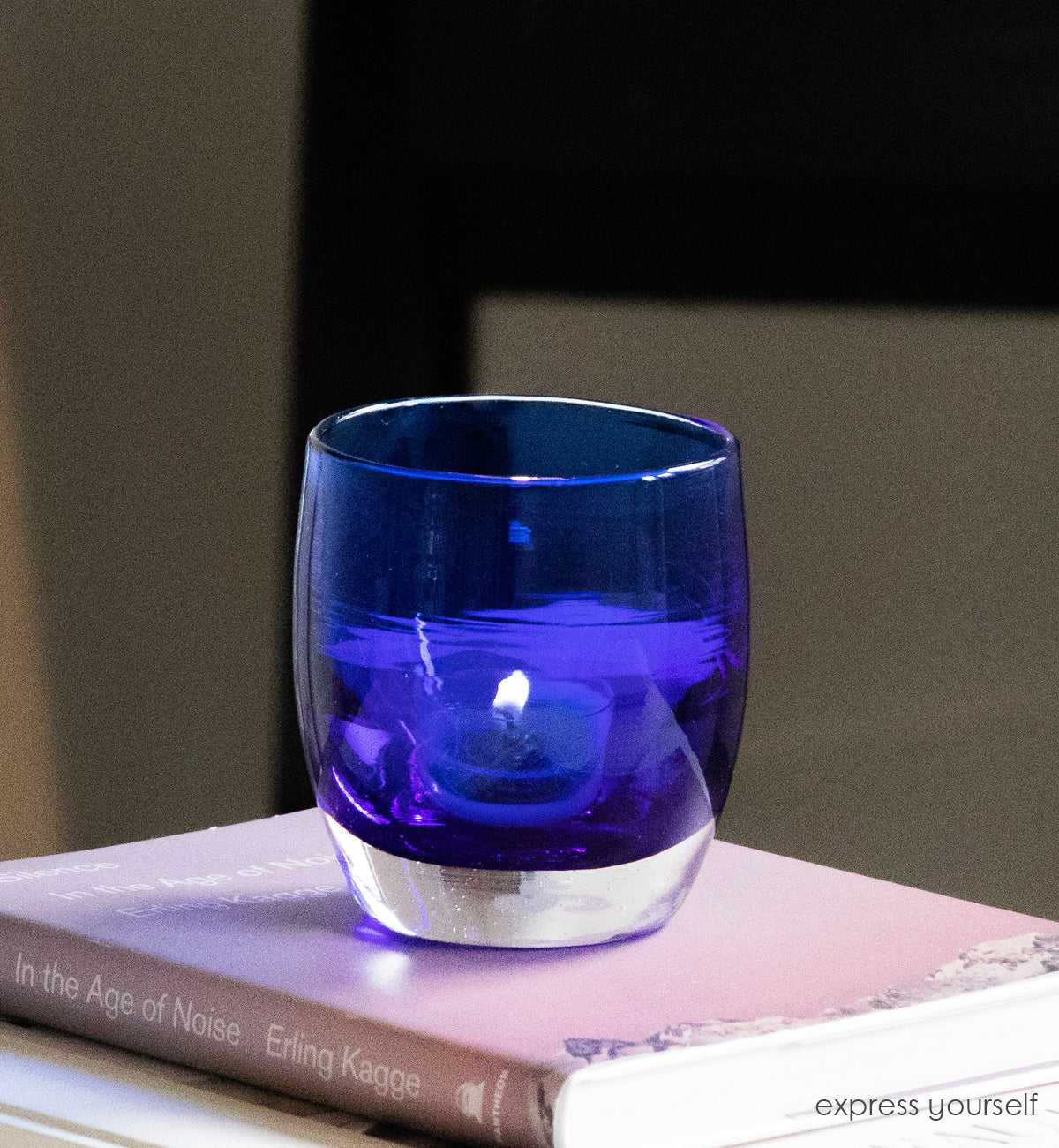 express yourself, transparent admiral blue, hand-blown glass votive candle holder sitting on a pink book.