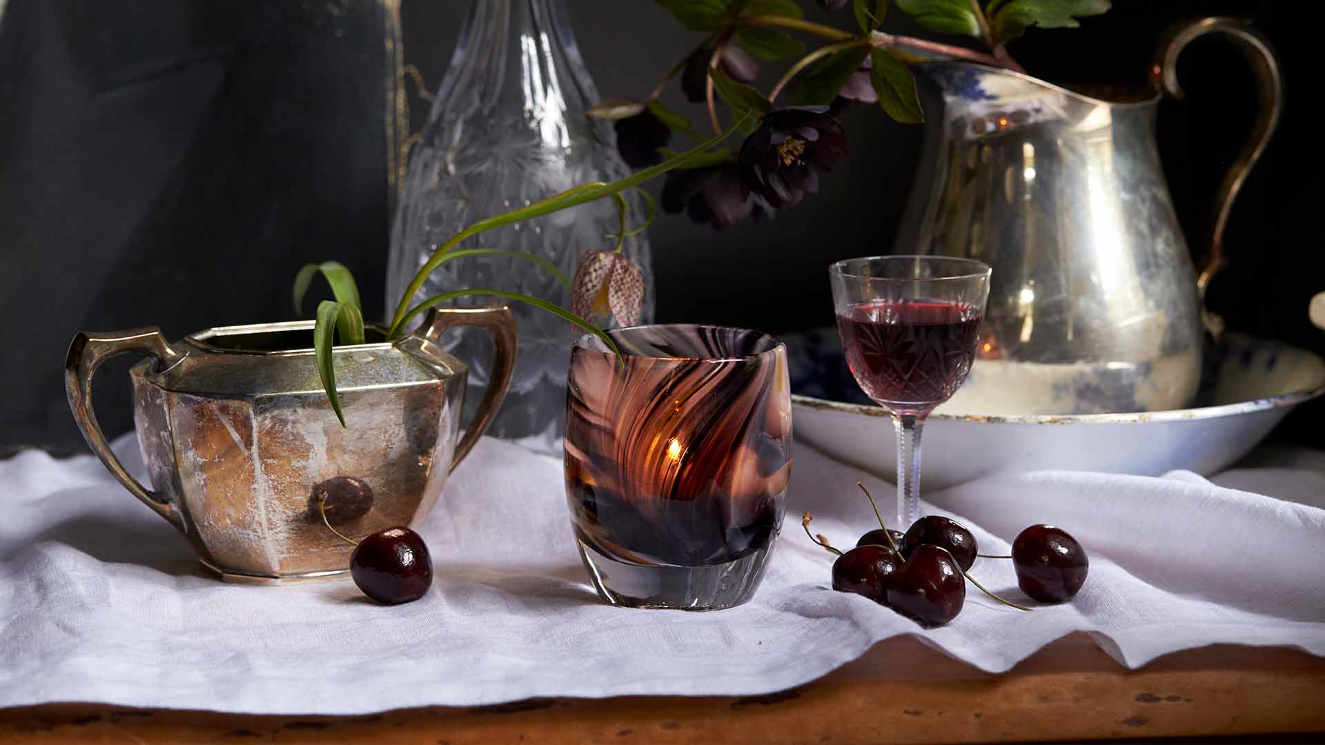 Exquisite a swirled merlot colored hand-blown glass votive candle holder, lit on an abundant dining table