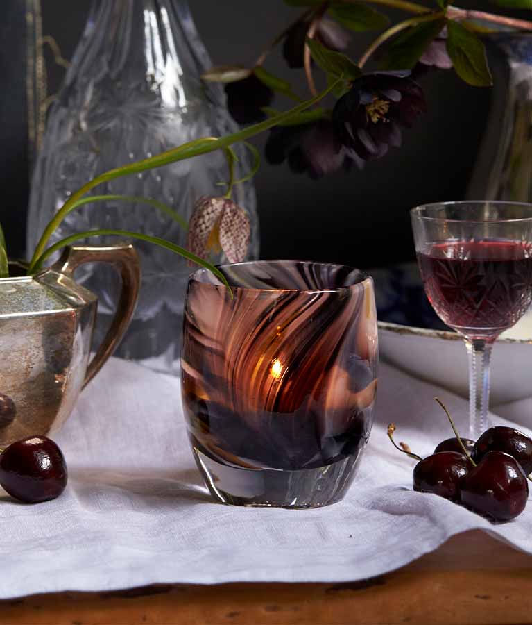 Exquisite a swirled merlot colored hand-blown glass votive candle holder, lit on an abundant dining table