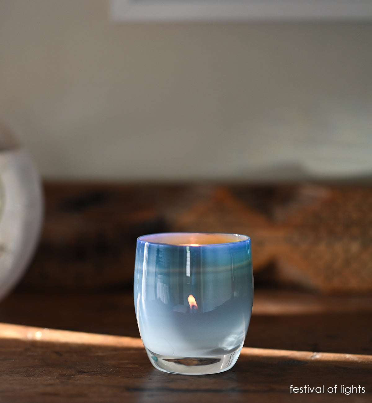 festival of lights blue white, hand-blown glass votive candle holder on a wood table with wood bench blurred in background.