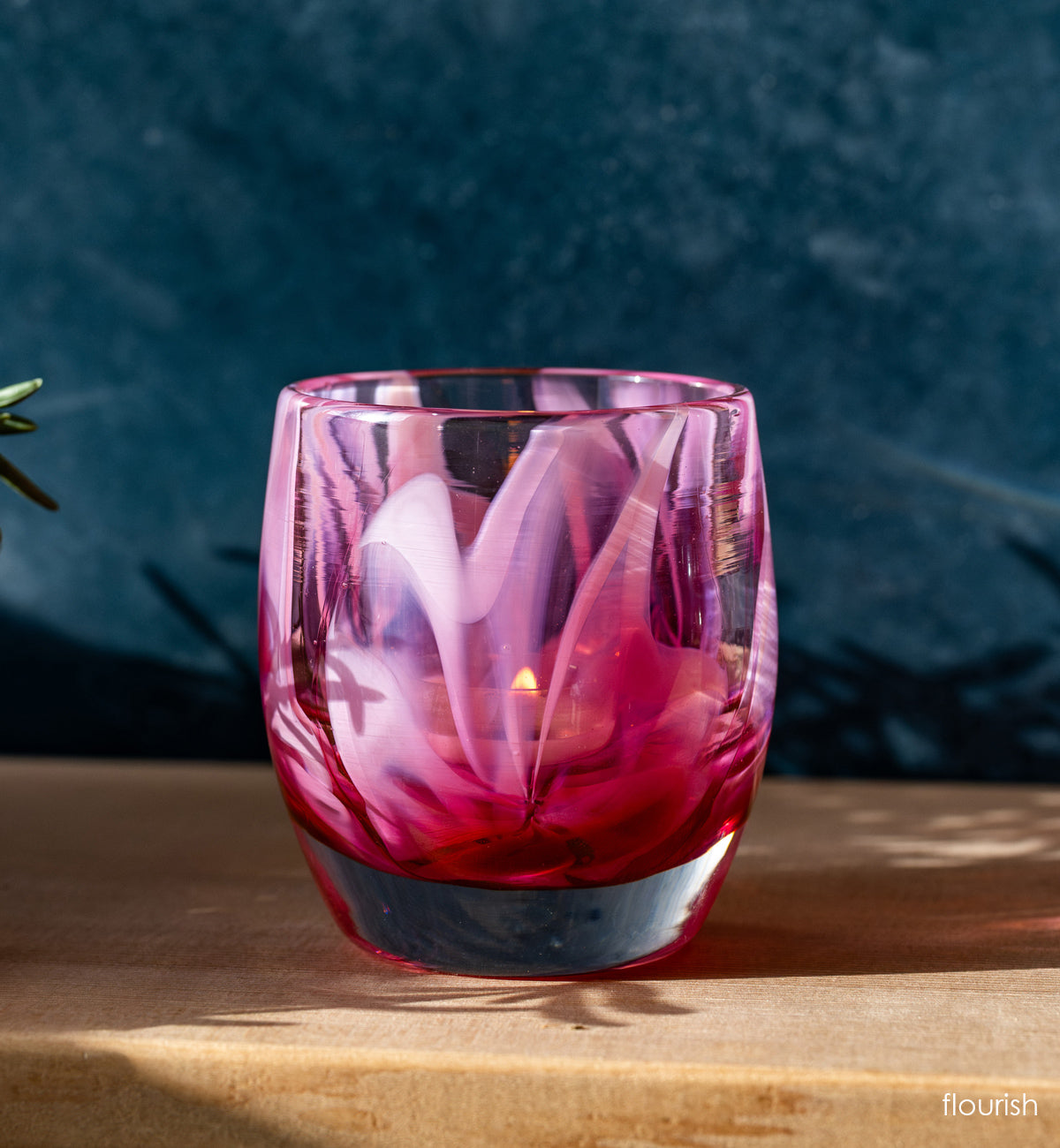 beautiful pink hand-blown glass murrini style candle holder on wood shelf.