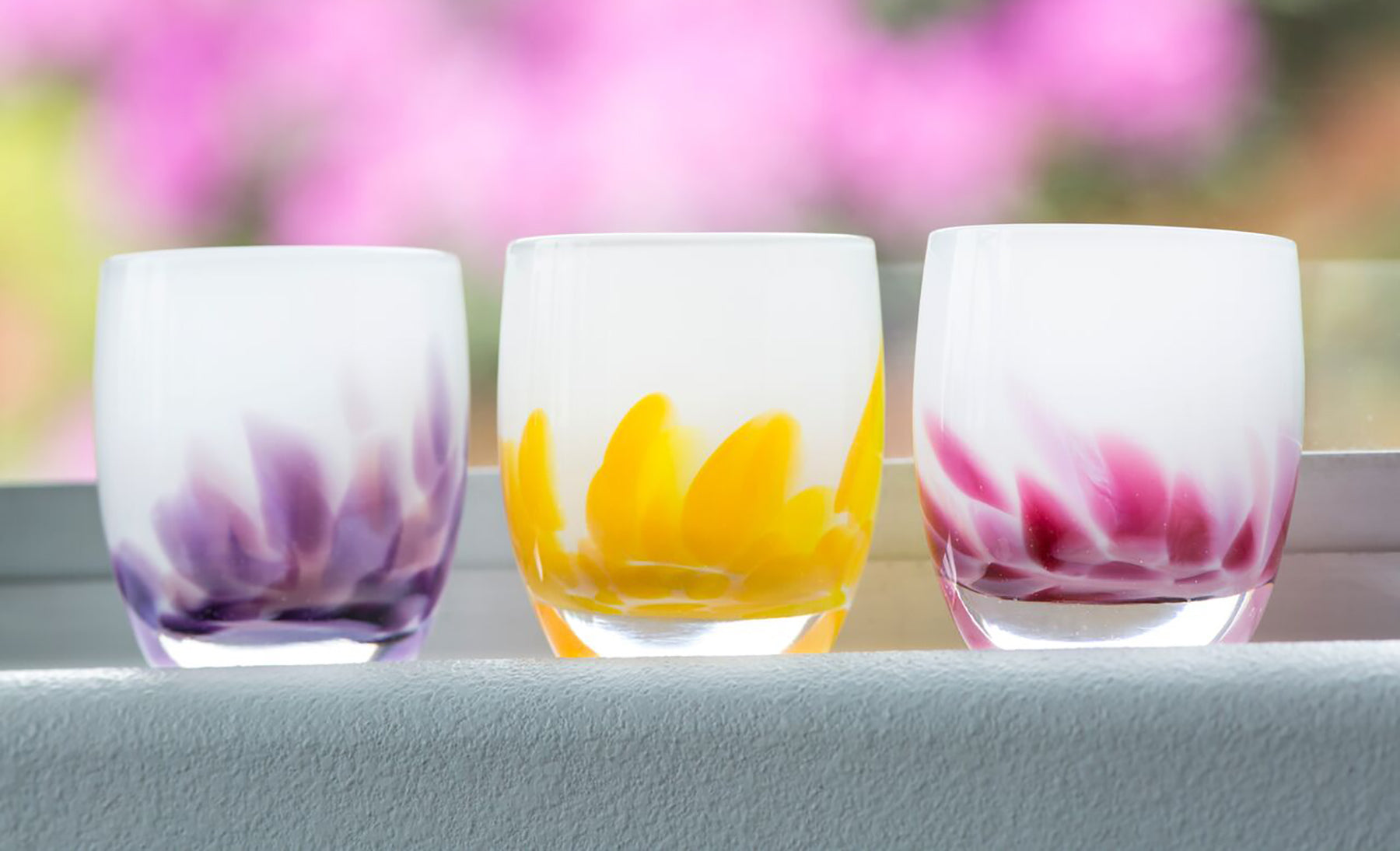 wisteria, buttercup and petal, handblown glass candle holders on a window sil.