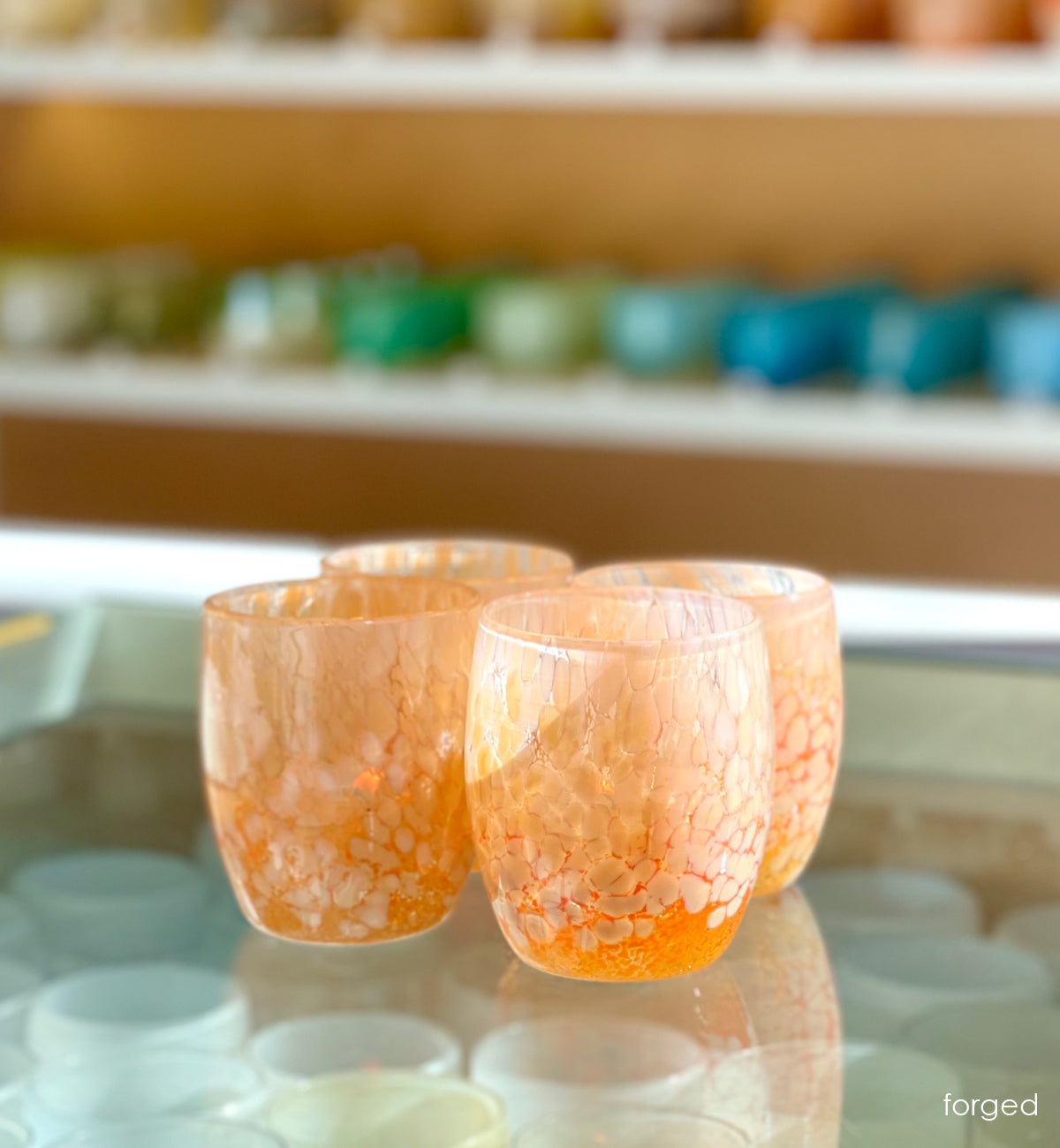 four 'forged' orange and white hand-blown glass candle holder on glass shelf in glassybaby shop.