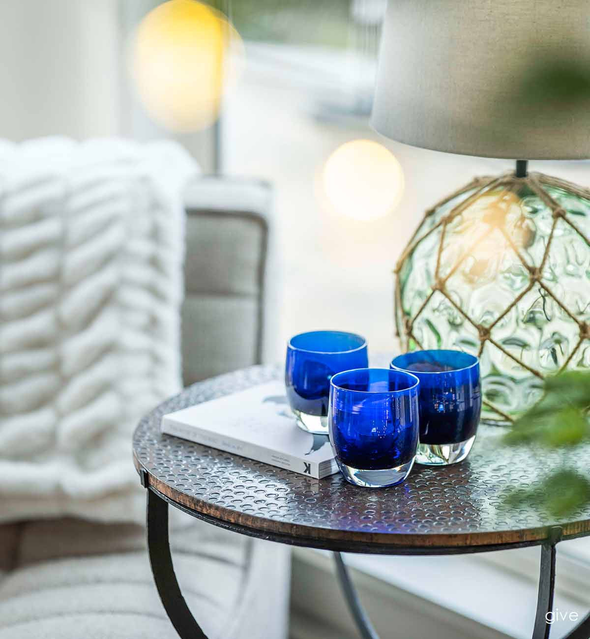 three give, hand-blown sapphire blue with silver metallic interior, hand-blown glass votive candle holders on a copper side table in a living room.
