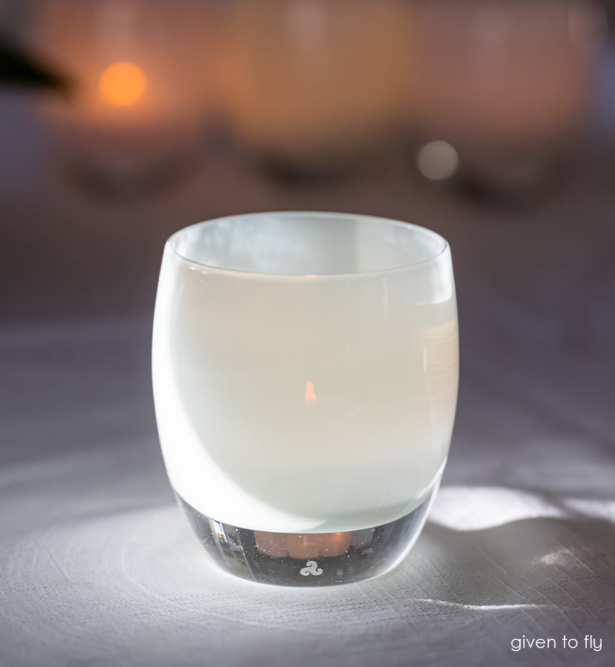 Candle in a glass candle holder on a reflective surface with a blurred background