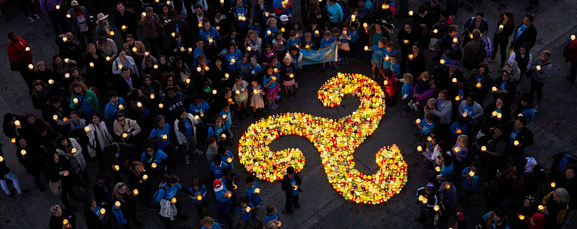 a birdseye view of a triskelion (glassybaby logo) lit by glassybaby being held by Montessori students at a giving event.