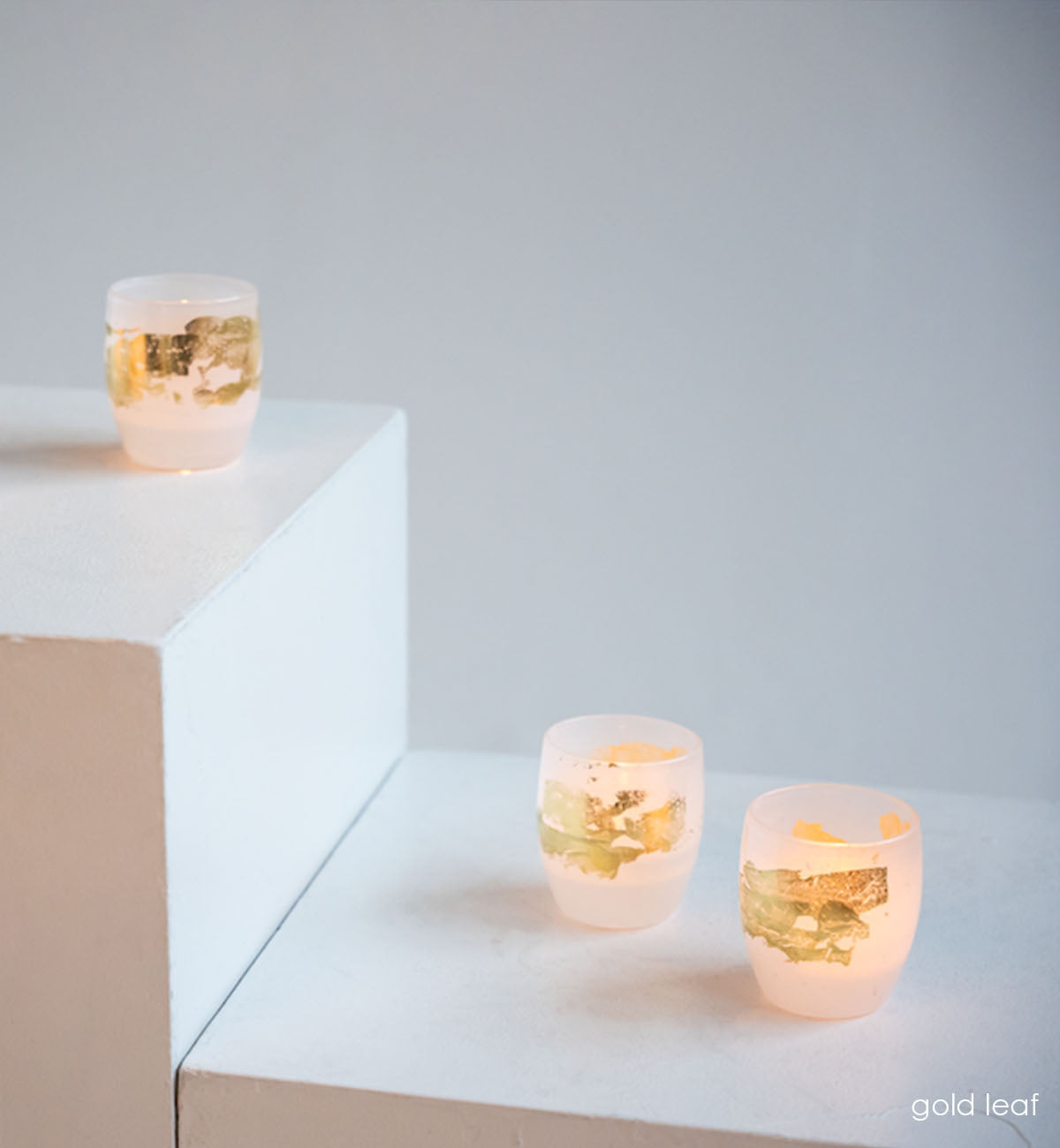 three gold leaf white with 24k gold hand-blown glass votive candle holders on white staggered surfacces.