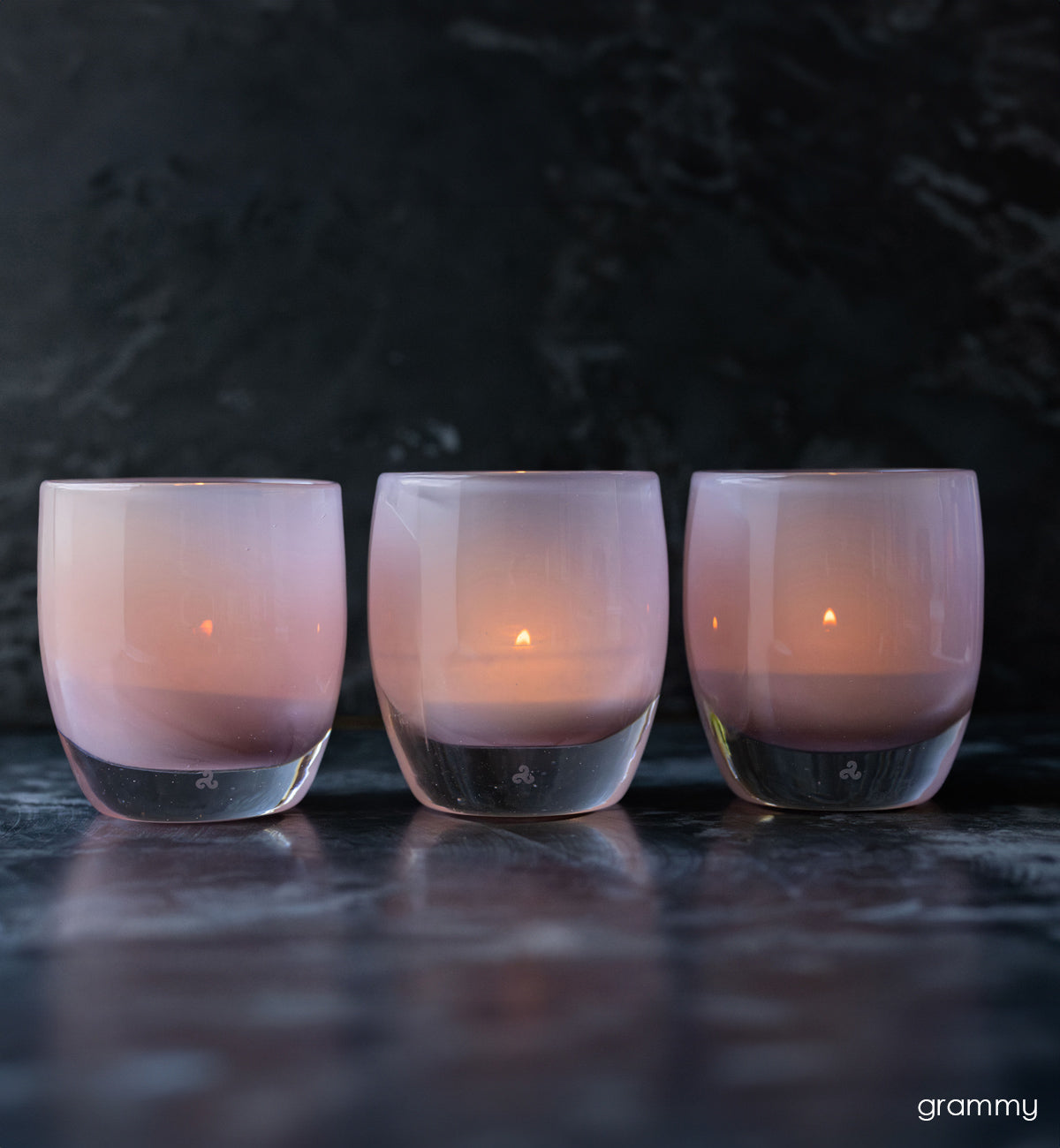 group of grammy, soft pink hand-blown glass votive candle holders on black backdrop.