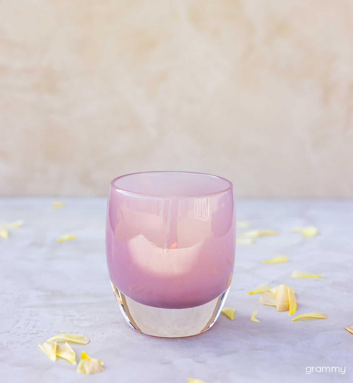 grammy, soft pink hand-blown glass votive candle holder. with yellow flower petals around it.