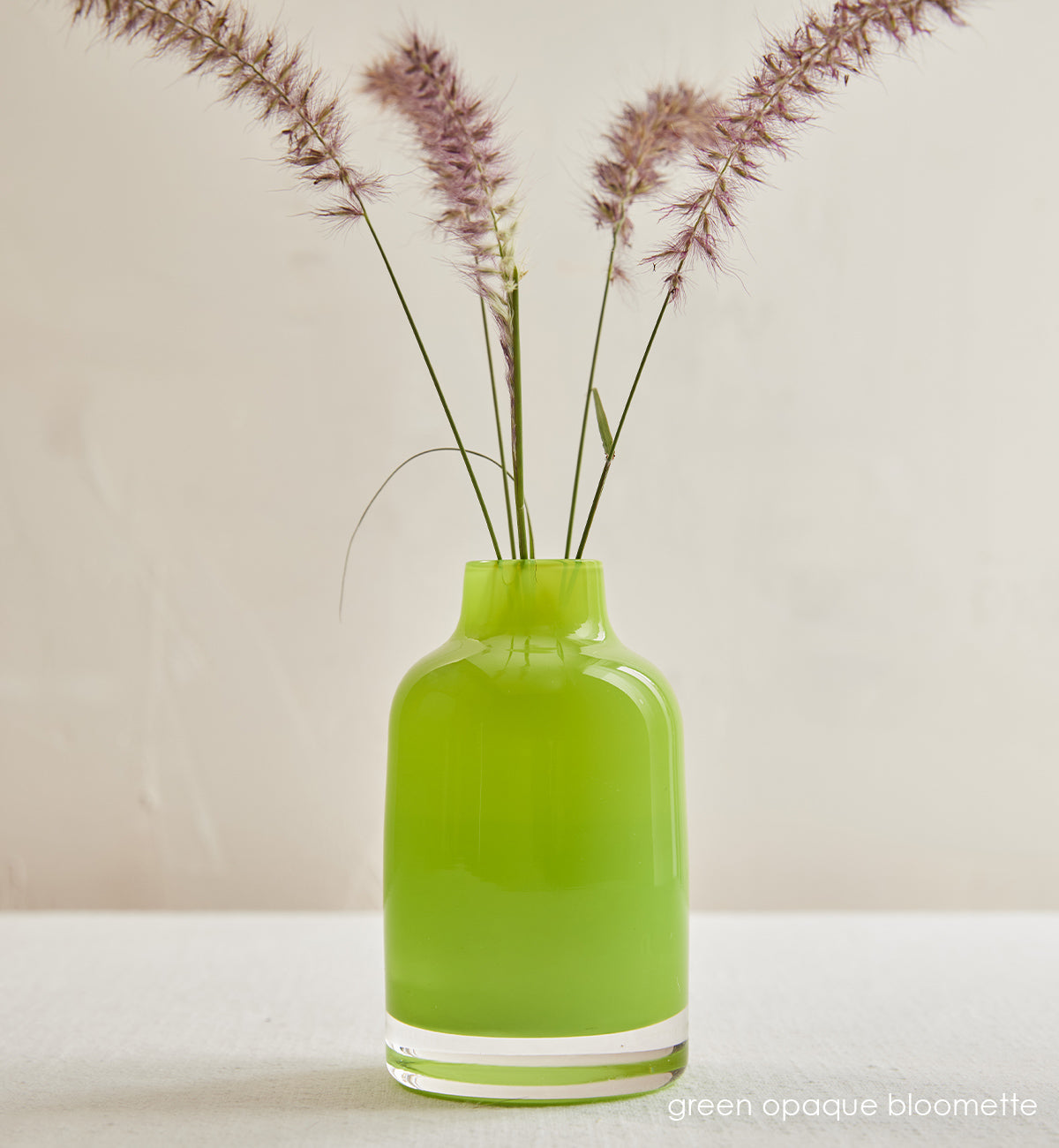 green opaque bloomette, lime green opaque hand-blown glass flower bud vase with purple grass in front of a cream background.