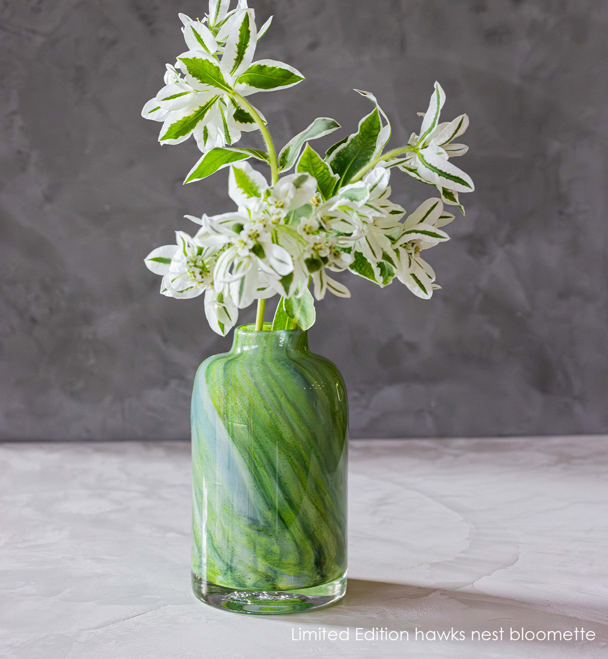 Limited Edition hawks nest bloomette vase green with blue swirls hold white flowers.