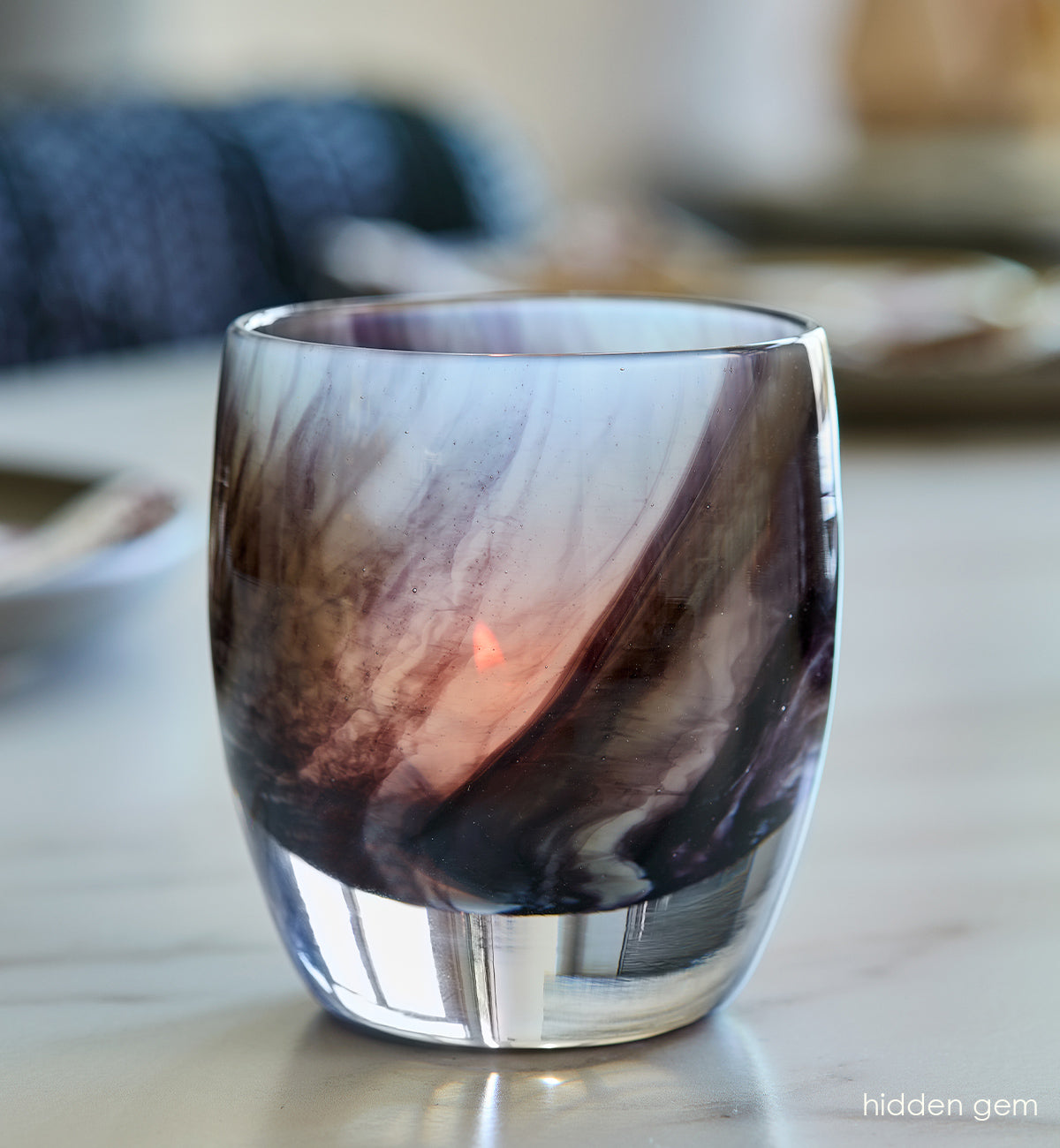 hidden gem, black white and grey ink like swirled hand-blown glass votive candle holder on a marble kitchen table with place settings blurred in background