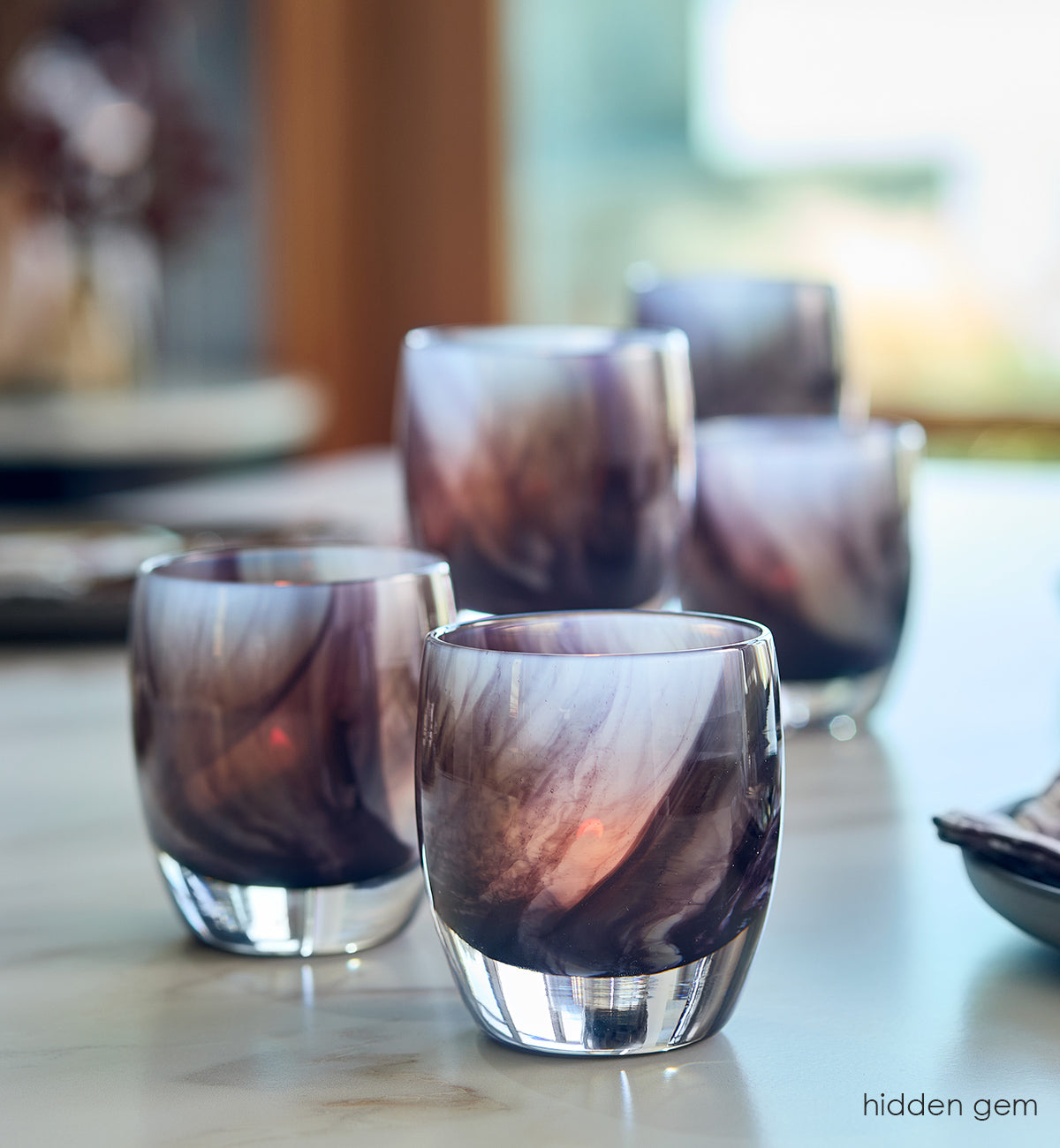 several hidden gem, black white and grey ink like swirled hand-blown glass votive candle holders on a marble dining room table.