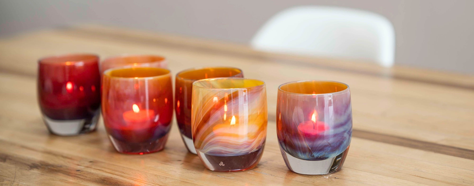 grouping of horoscope purple orange cranberry, hand-blown glass votive candle holders on a light wood table.