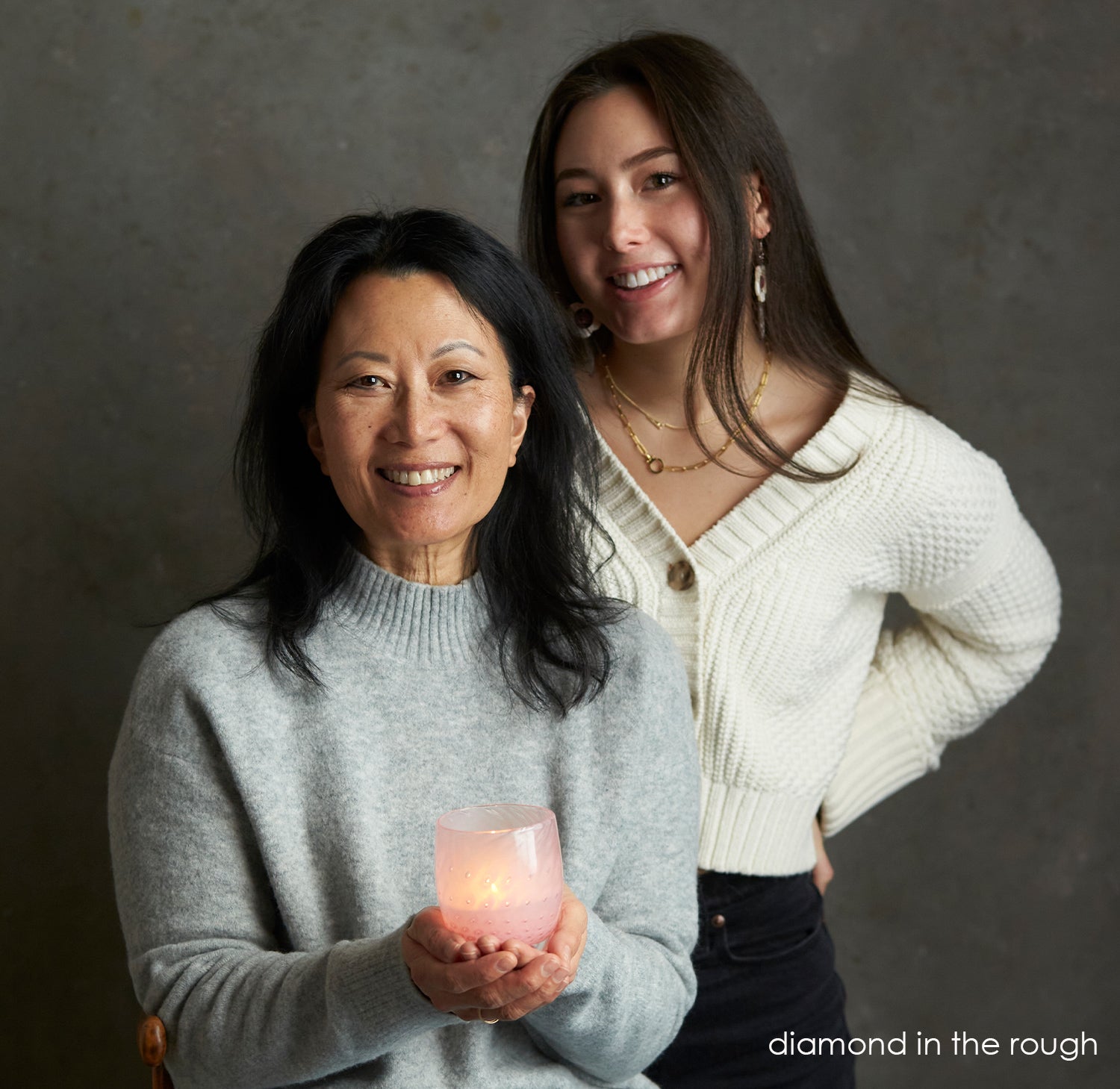 mother daughter duo, jeanne and amanda holding the hand blown glass candle holder - diamond in the rough - pink with a bubble pattern.