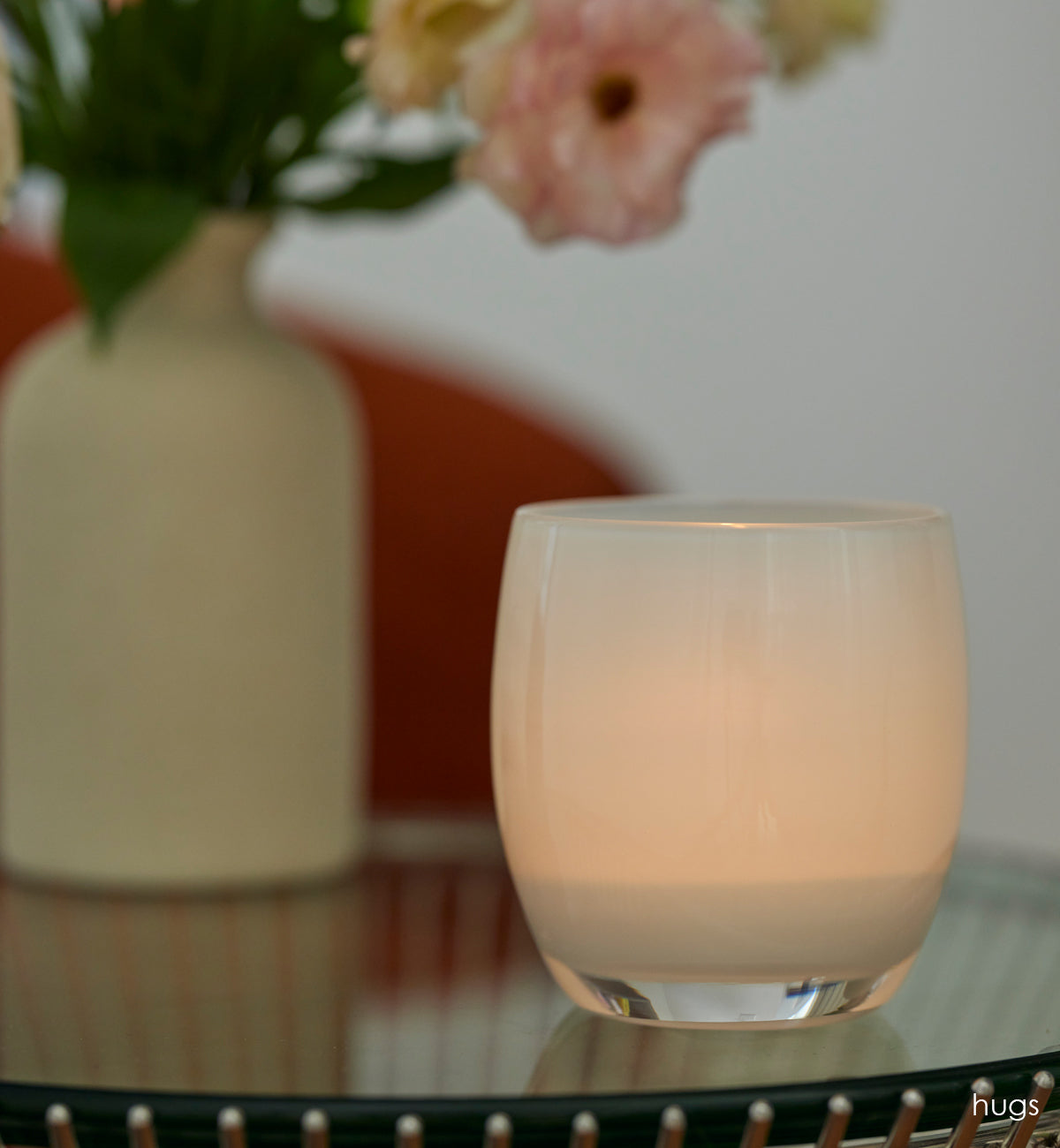 hugs opaque off white hand-blown glass votive candle holder on a table with a white ceramic vase.