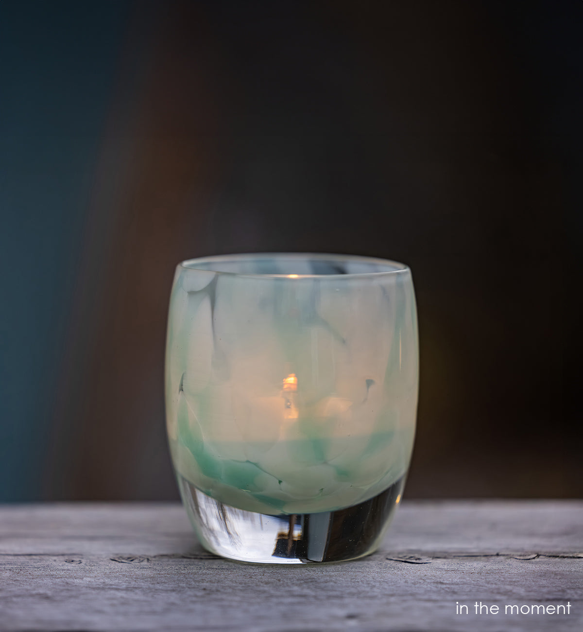 in the moment, blue, white, hand-blown glass votive candle holder with a lit candle on a wooden surface, dark background