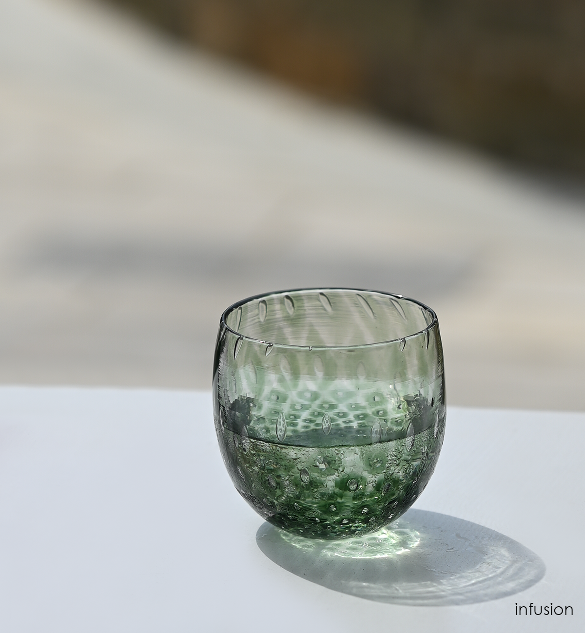 infusion, dark green hand-blown drinking glass with a bubble pattern on a white surface in the sunlight.