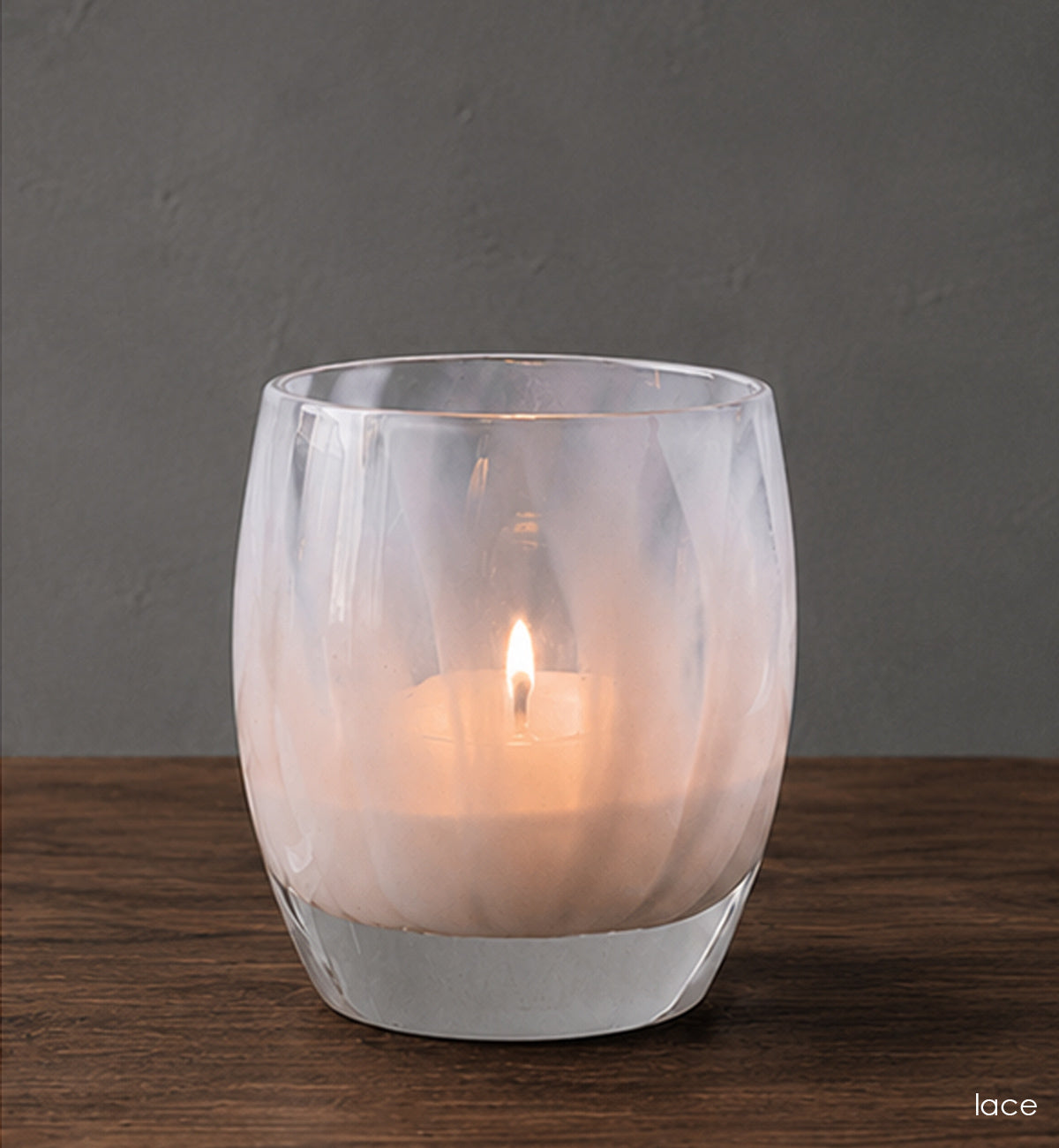 Glass candle holder with a lit candle on a wooden surface and gray background