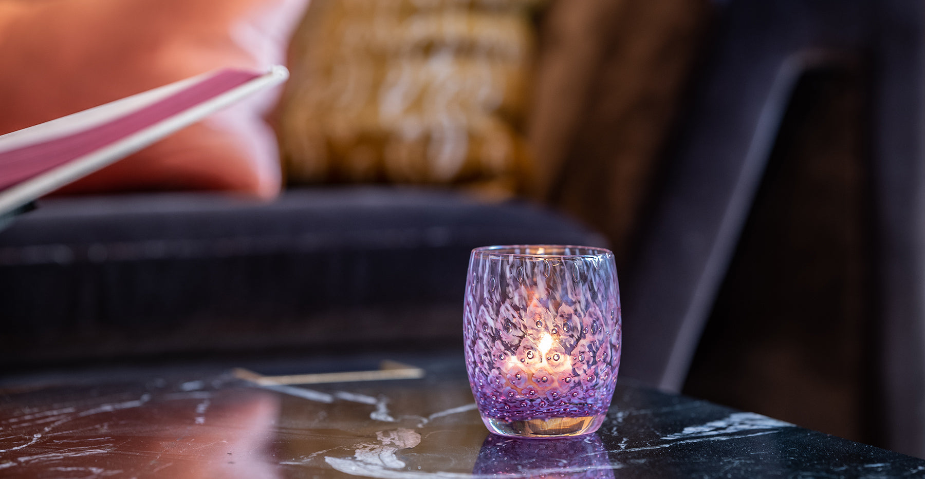 lady, a purple hand-blown glass candle holder with bubble pattern sitting on a marble table