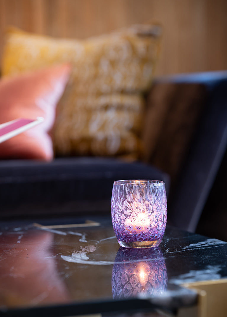 lady, a purple hand-blown glass candle holder with bubble pattern sitting on a marble table