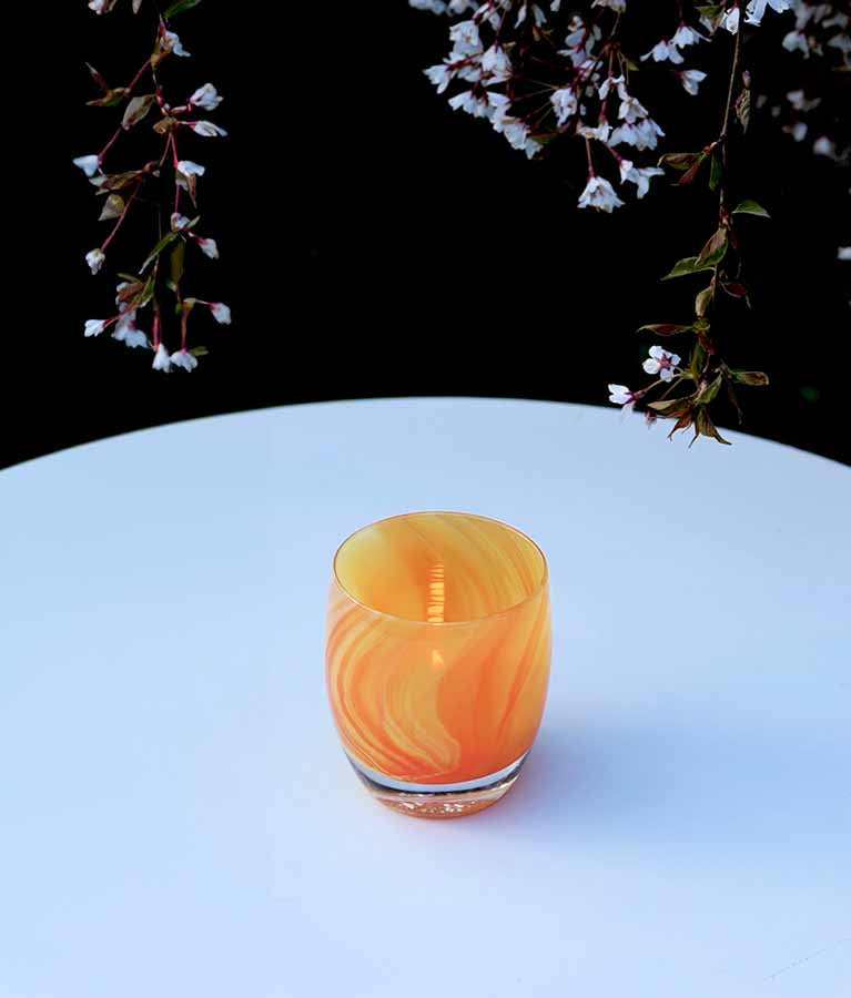 lifesaver sitting on a round white table in the garden. Marbled orange hand-blown glass votive candle holder.